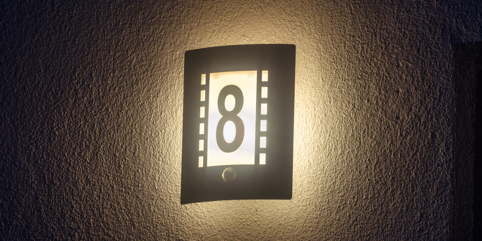 An illuminated house number on a white wall.